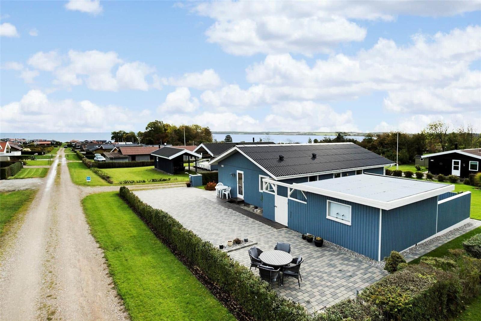 Blau gestrichenes Ferienhaus mit Terrasse und Garten. Blick auf Wasser und Himmel.