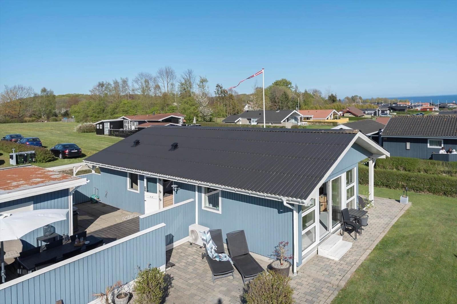 Blau gestrichenes Haus mit Terrasse und Garten. Flagge weht über dem Dach.