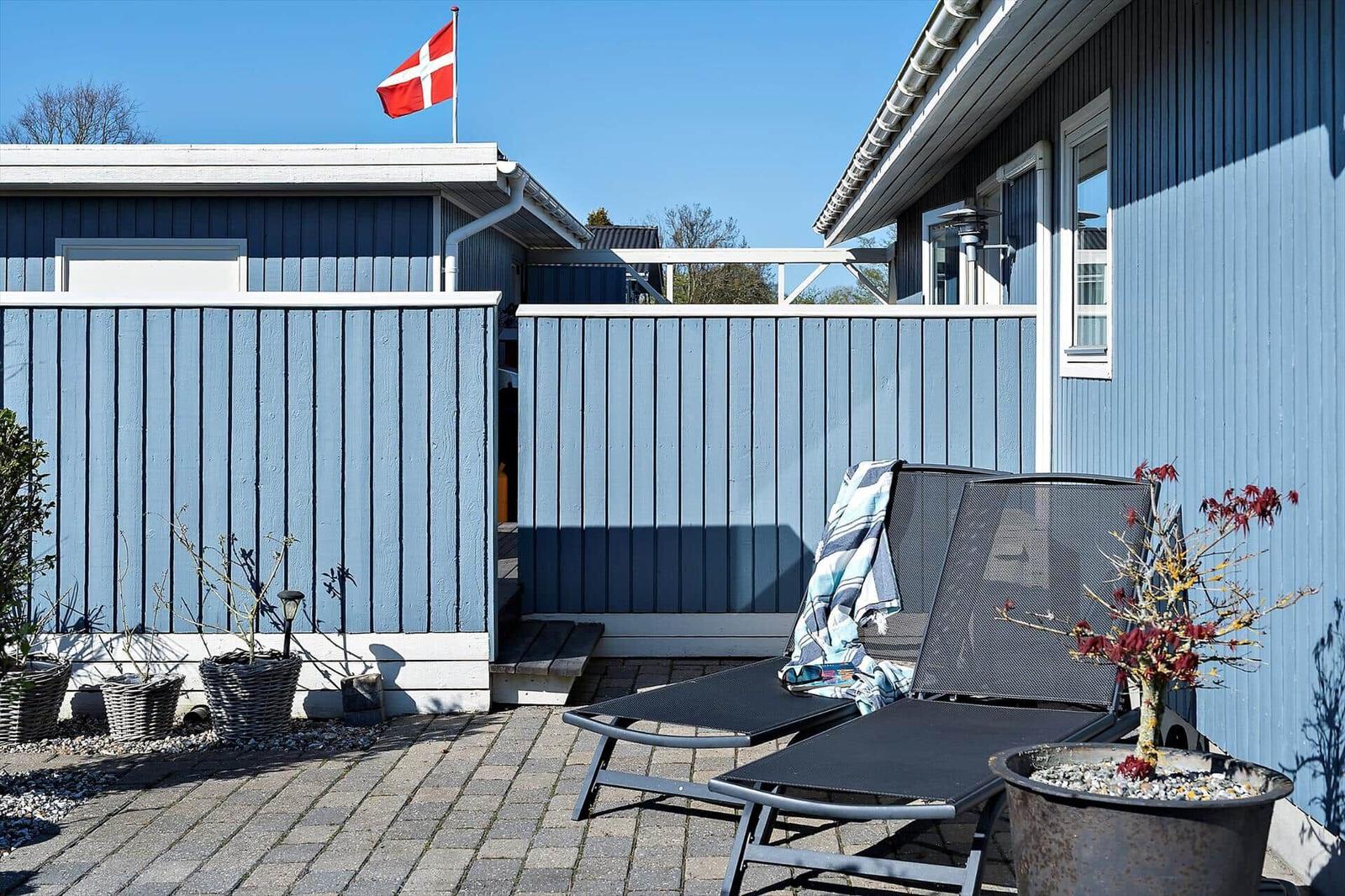 Terrasse mit Liegestühlen, blauer Holzwand und dänischer Flagge.
