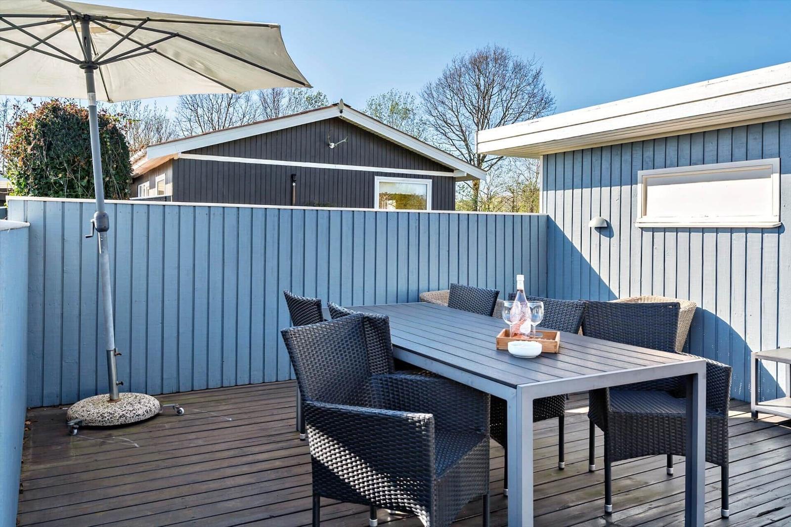Terrasse mit Tisch, Stühlen und Sonnenschirm. Holzdecke und blaue Wand.