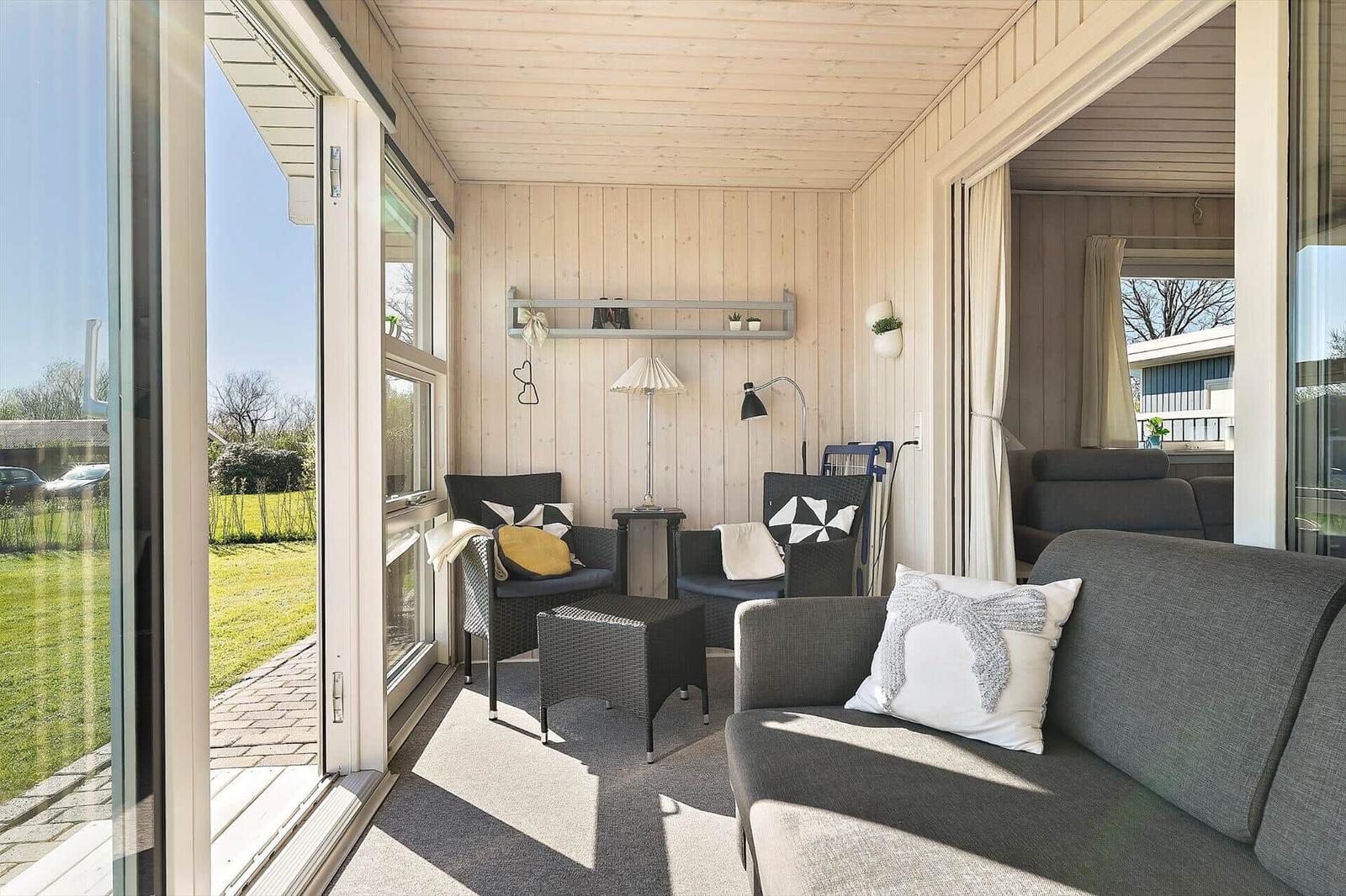 Terrasse mit Sitzgruppe, Glaswänden und Blick auf Garten.