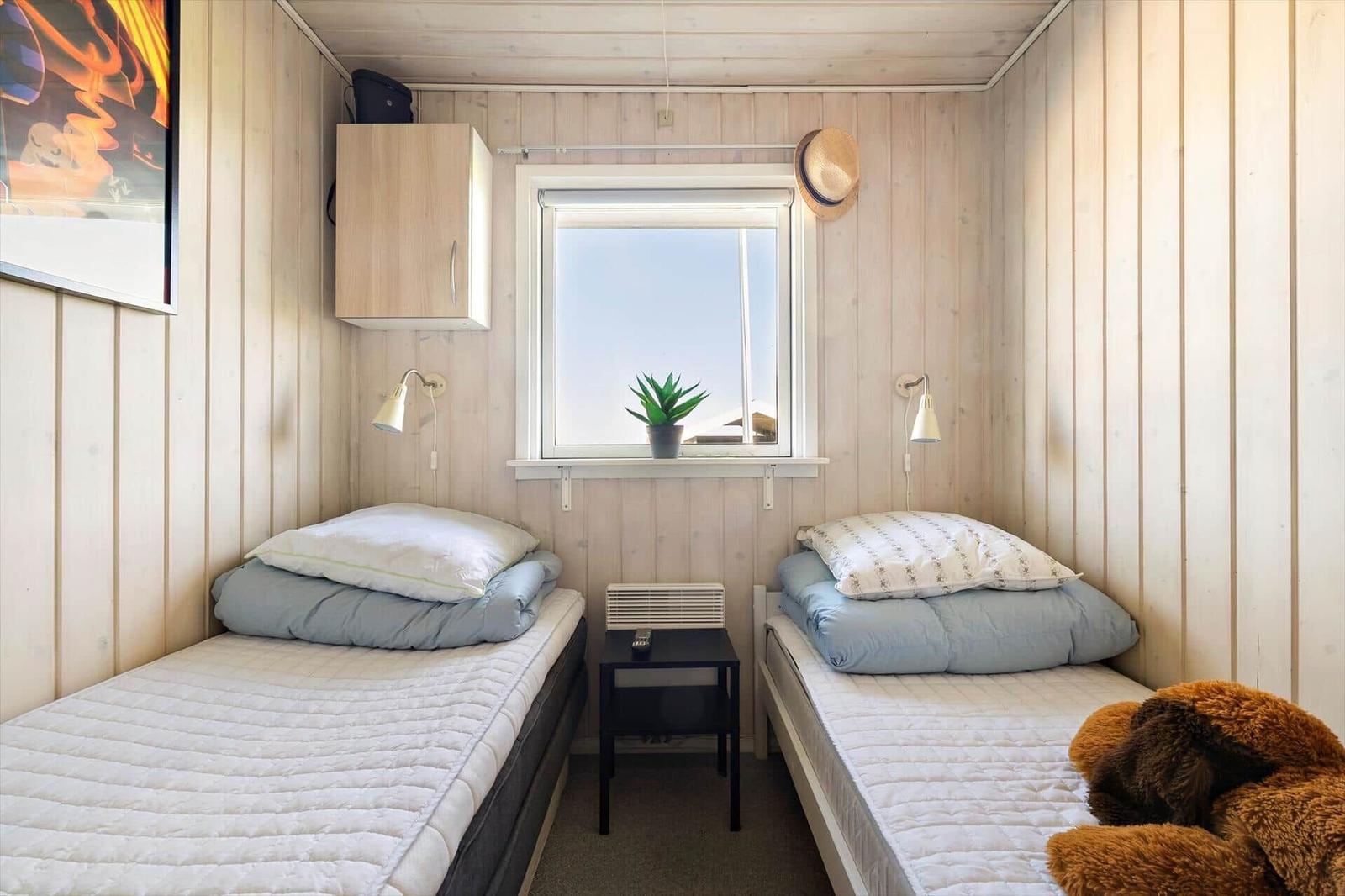 Zwei Einzelbetten mit Matratzen und Kissen. Fenster mit Pflanze. Holzwand und Nachttisch.