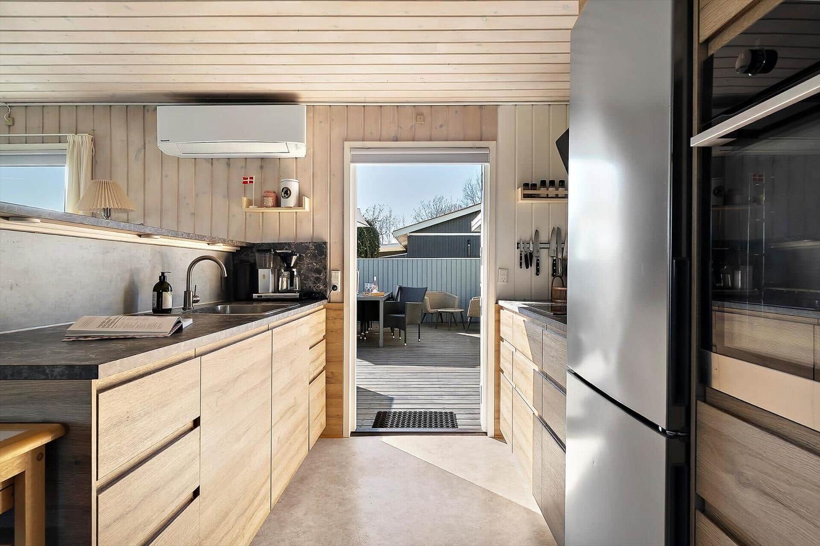 Küche mit Holzschränken, Kühlschrank und Blick auf die Terrasse.