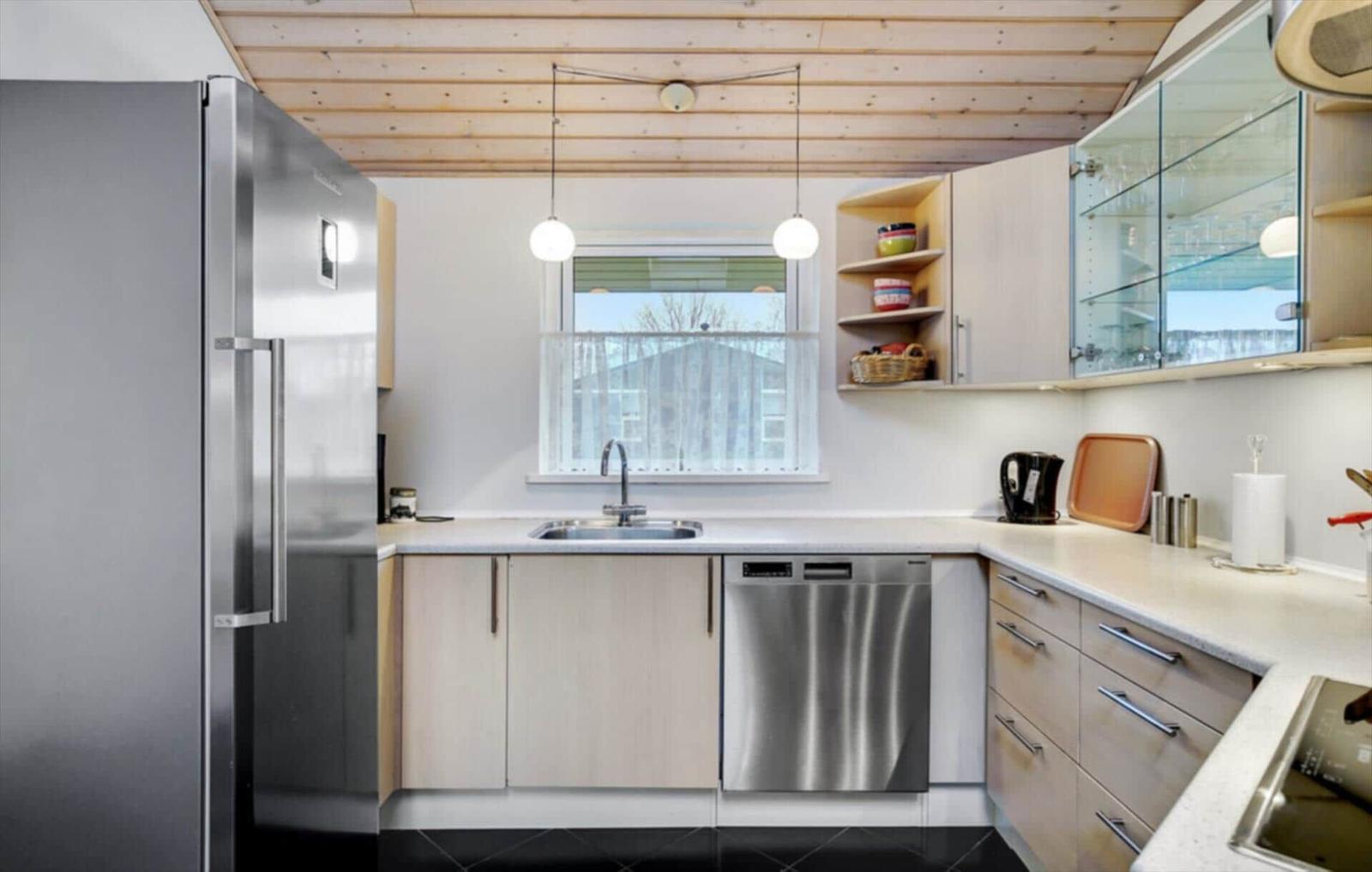 Kitchen with stainless steel fridge and dishwasher, wooden ceiling, and window with outside view.