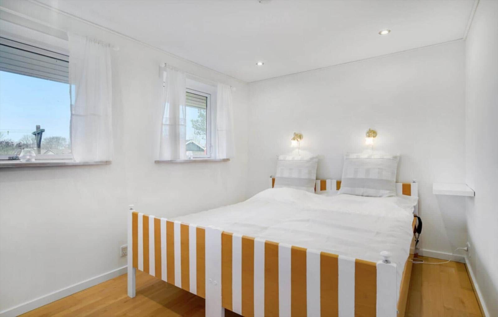 Bedroom with double bed, two windows, and wooden floor.