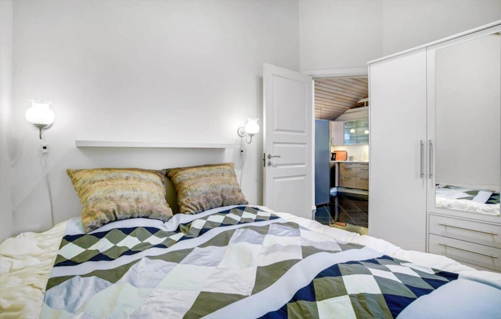 Bedroom with bed, nightstand, and wardrobe. Corridor to kitchen visible.
