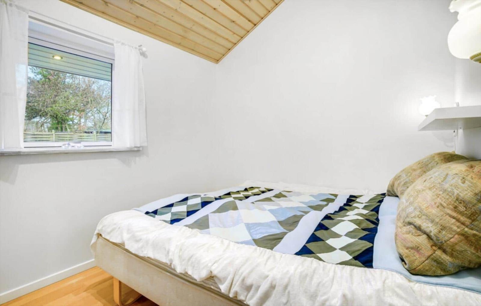 A bedroom with bed, window, and wooden ceiling.