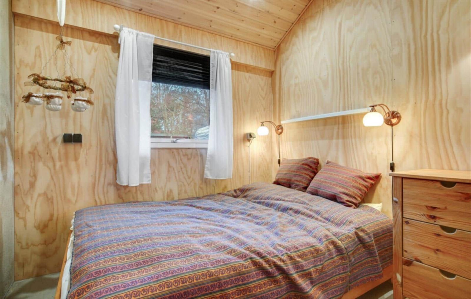 Bedroom with wooden walls, bed, nightstand, and window with curtains.