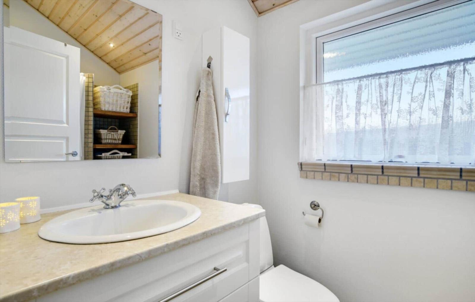 Bathroom with sink, mirror, and window with curtain.