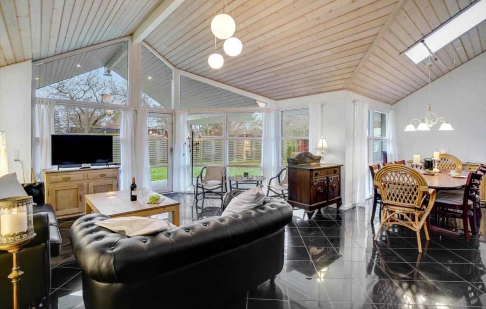 Large living and dining area with black floor, wooden ceiling, and ample windows.