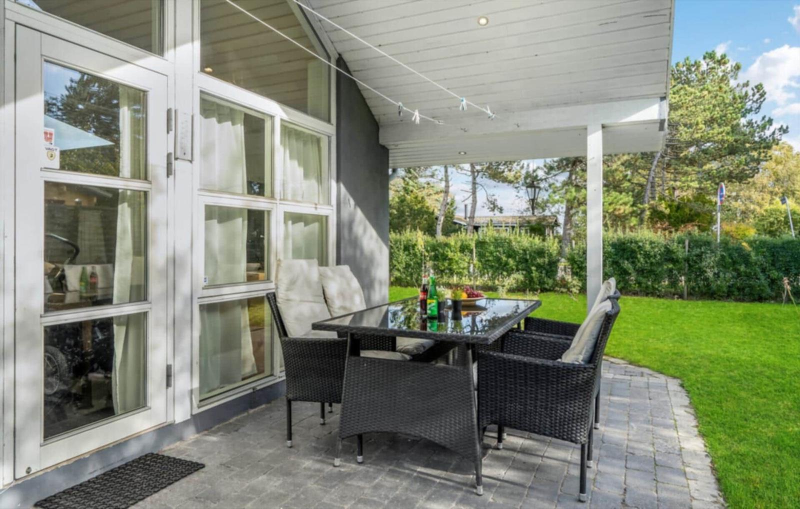 Patio with seating group and table under roof. Lawns and trees in background.