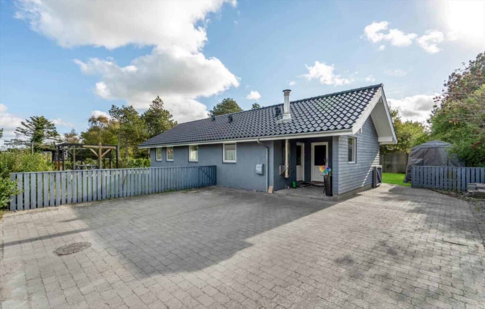 A gray house with roof and yard. Surrounded by trees and a fence.