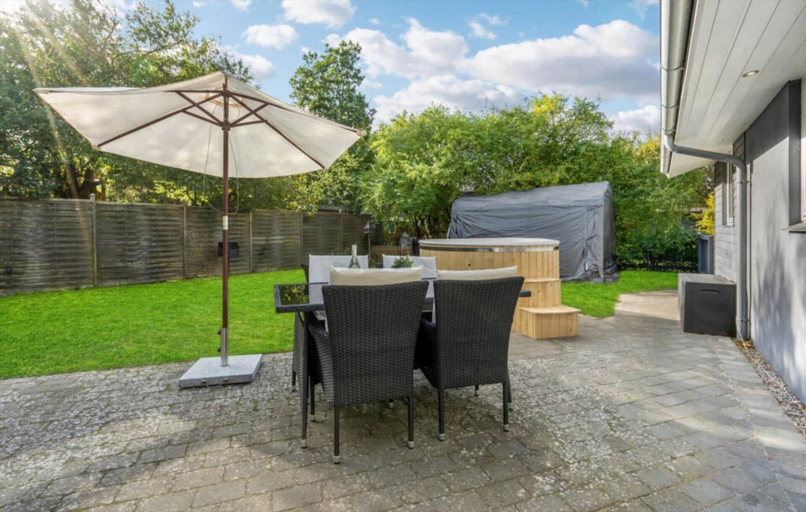 Terrace with seating, umbrella, and hot tub in the background.
