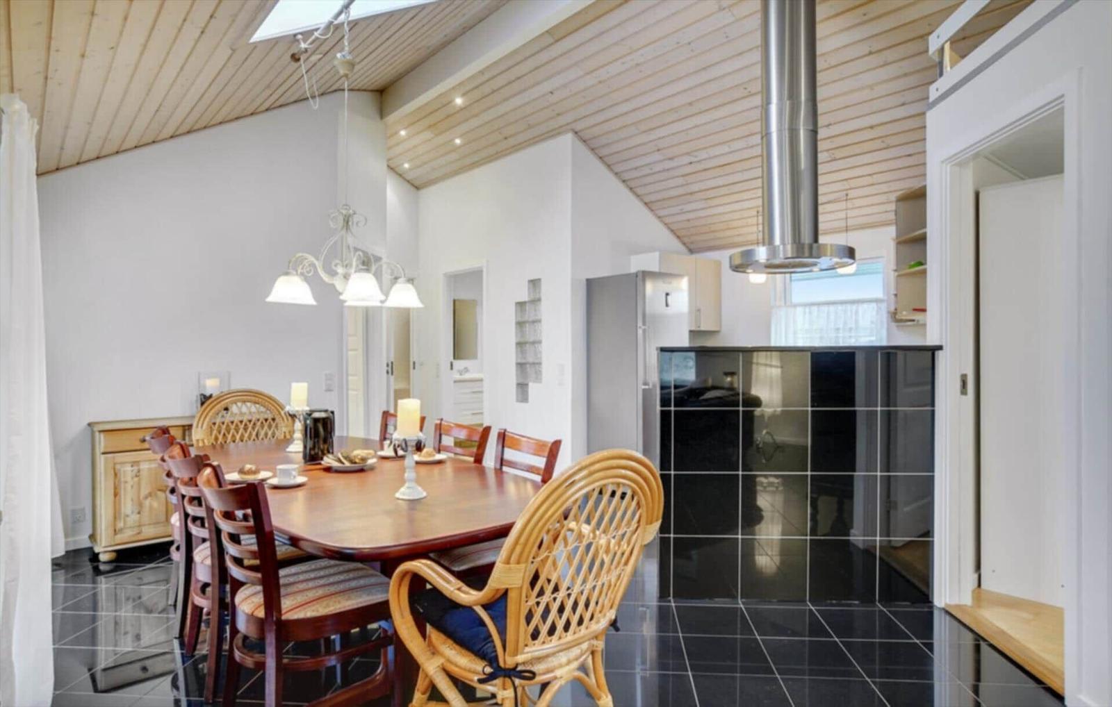 Dining area with wooden table and chairs, kitchen with black tiles and stainless steel hood.