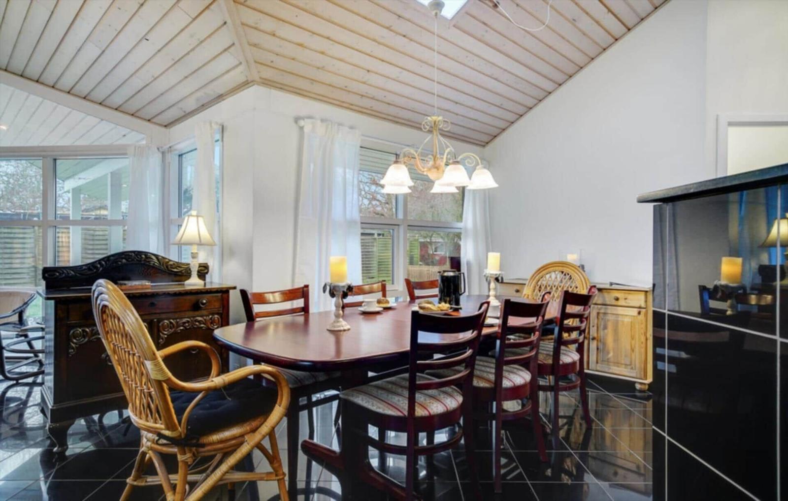 Dining room with round table, chairs, and windows. Wooden ceiling and black tiles.