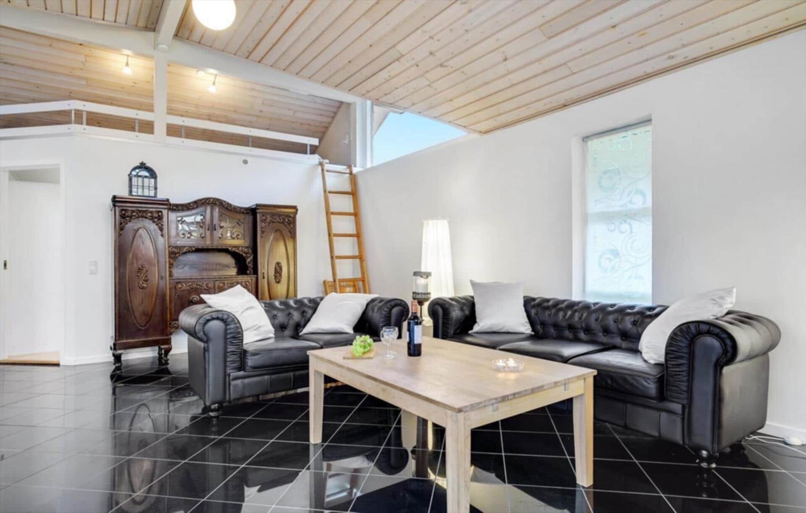 Living room with two black leather sofas, wooden table, and dark floor. Wooden mezzanine area with ladder.
