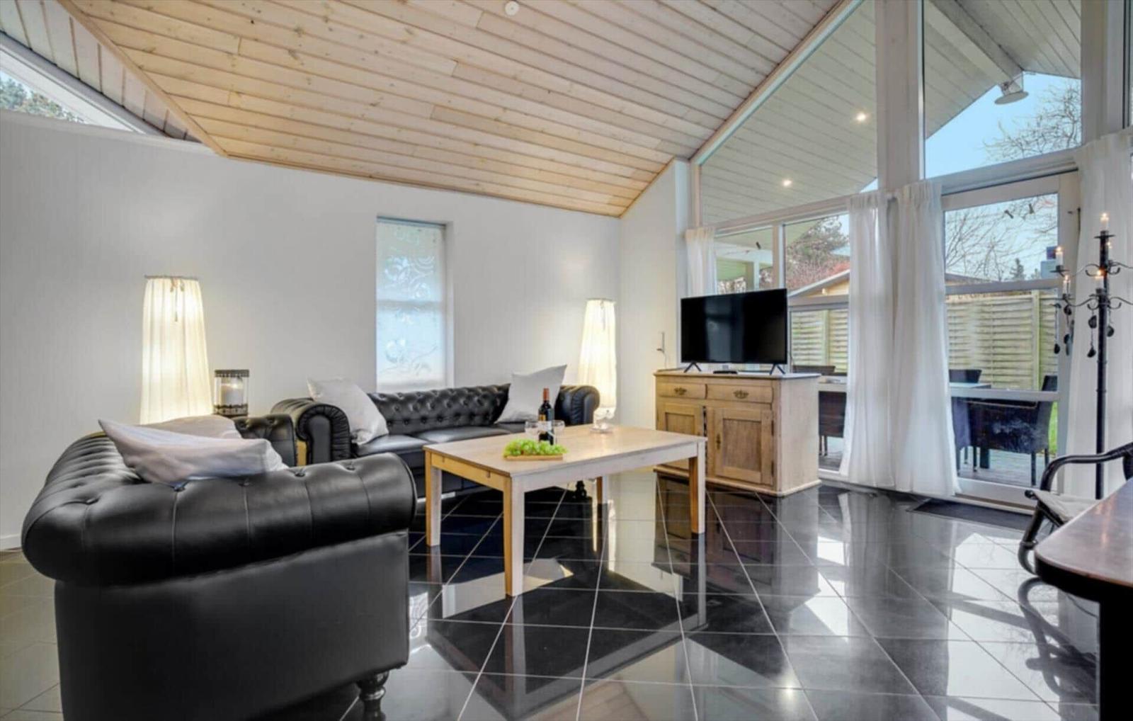 Living room with leather sofa, wooden table, and TV. Black tiles and wooden ceiling.
