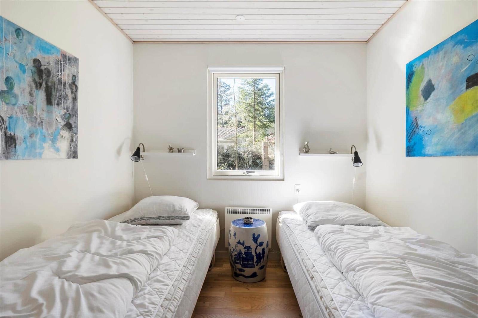 Two beds with white bedding face a window with a view of trees.