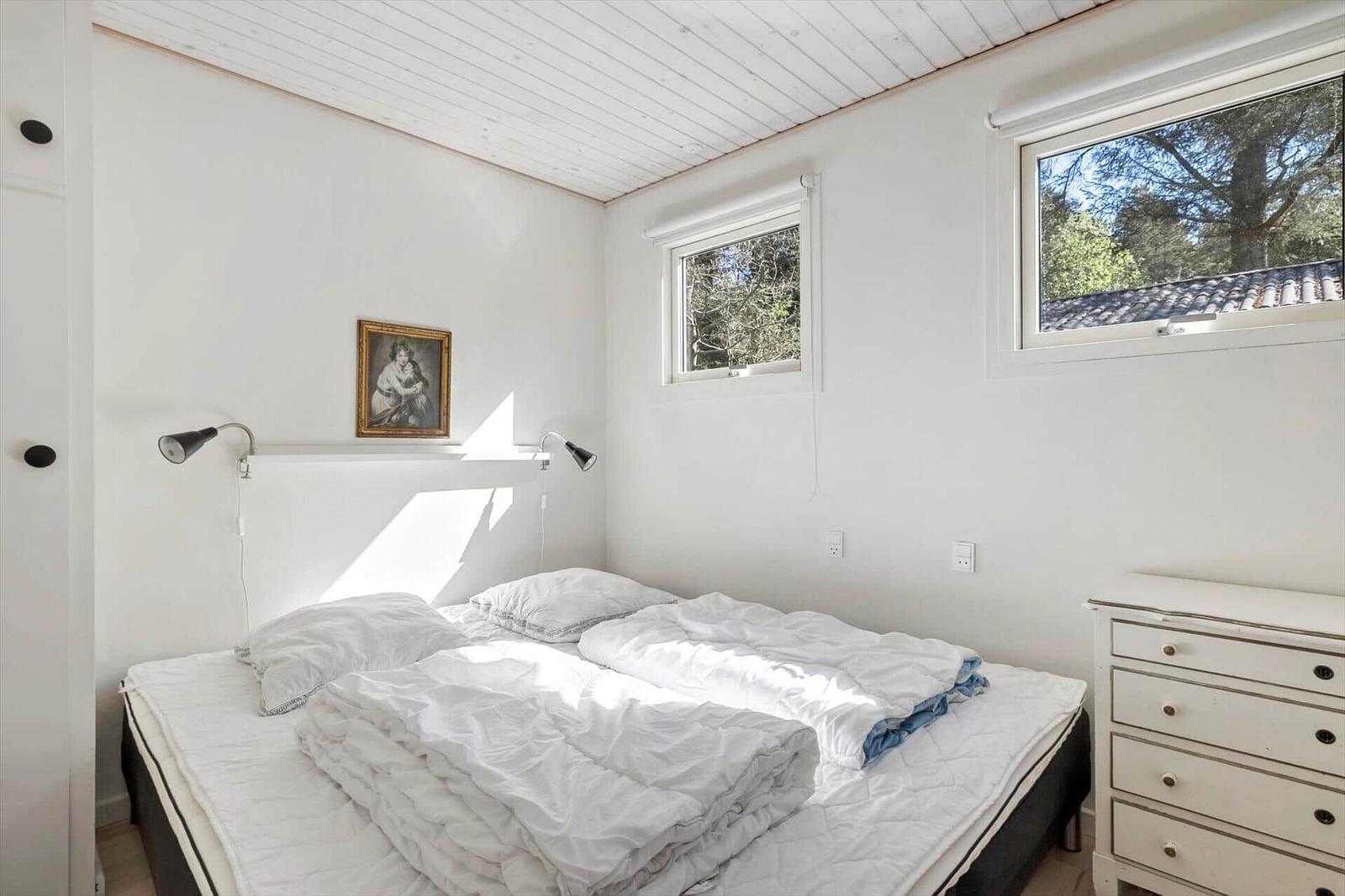 Bedroom with bed, dresser, and windows. Wooden ceiling and wall picture.