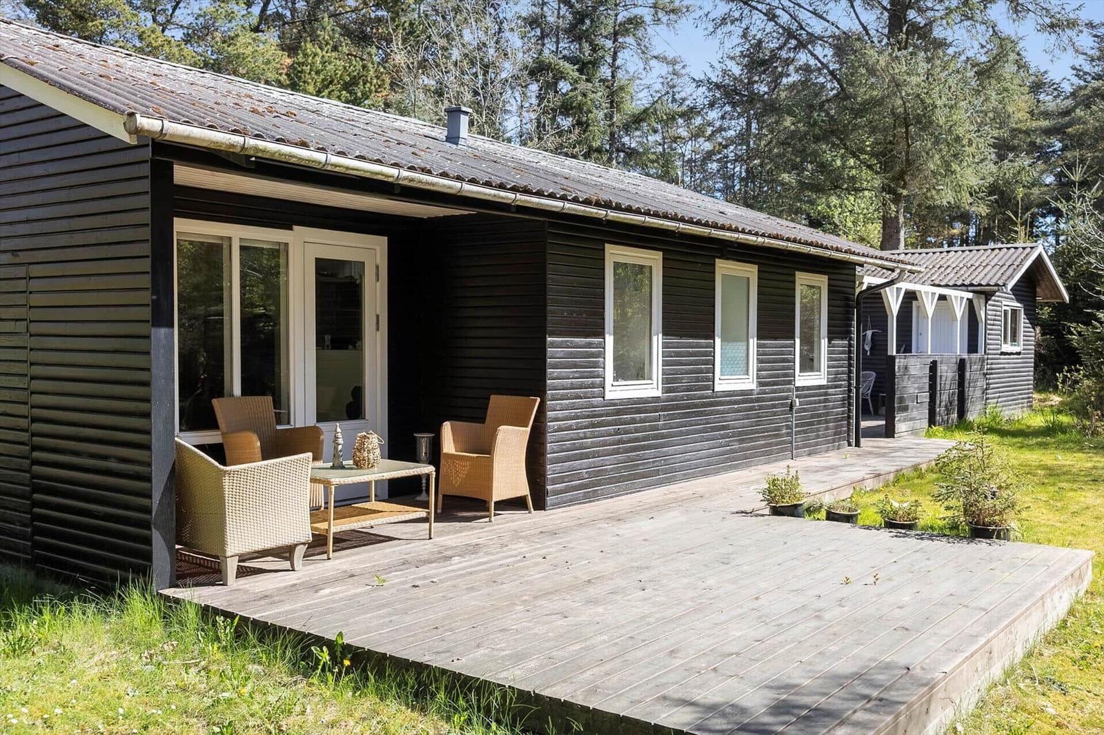 Black wooden cabin with terrace and garden. Visible: windows, door, and garden furniture.