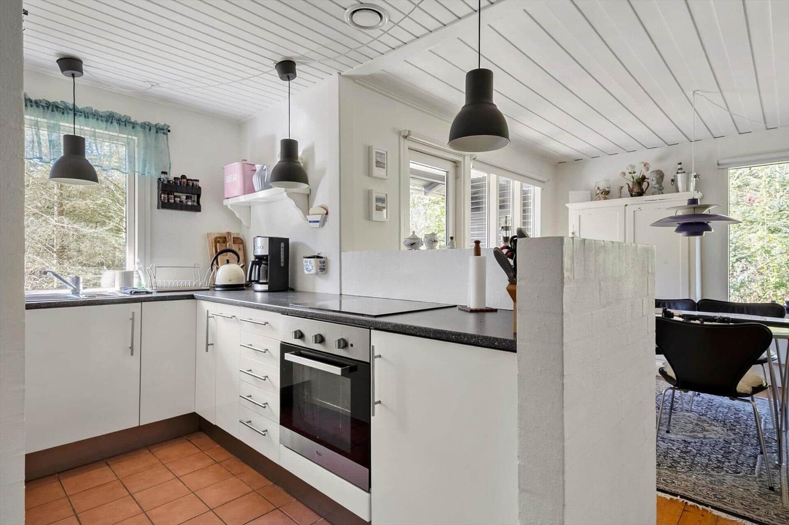 Kitchen with white cabinets, dark countertop, and windows with view of nature.