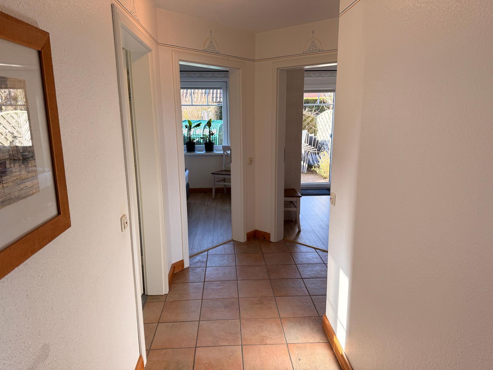 Flur mit Fliesenboden und Blick in Wohn- und Essbereich mit Fenster und Pflanzen.