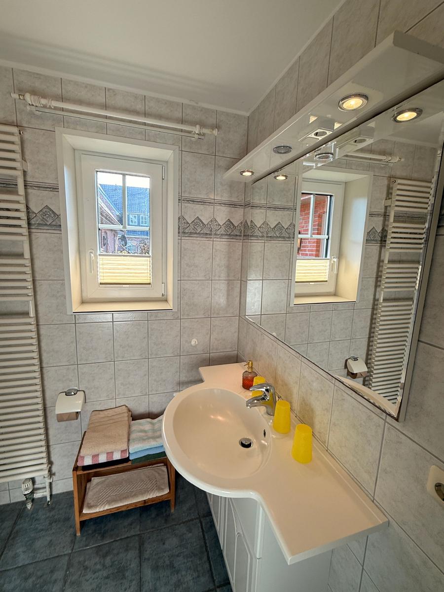 Bad mit Waschbecken, Spiegel und Fenster. Handtuchständer und Heizung sind vorhanden.