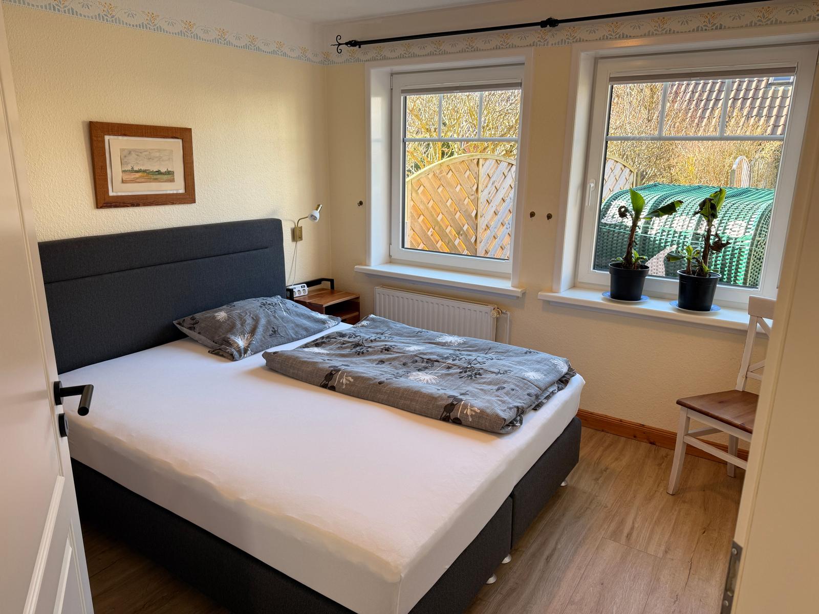 Schlafzimmer mit Bett, Fenstern und Pflanzen.