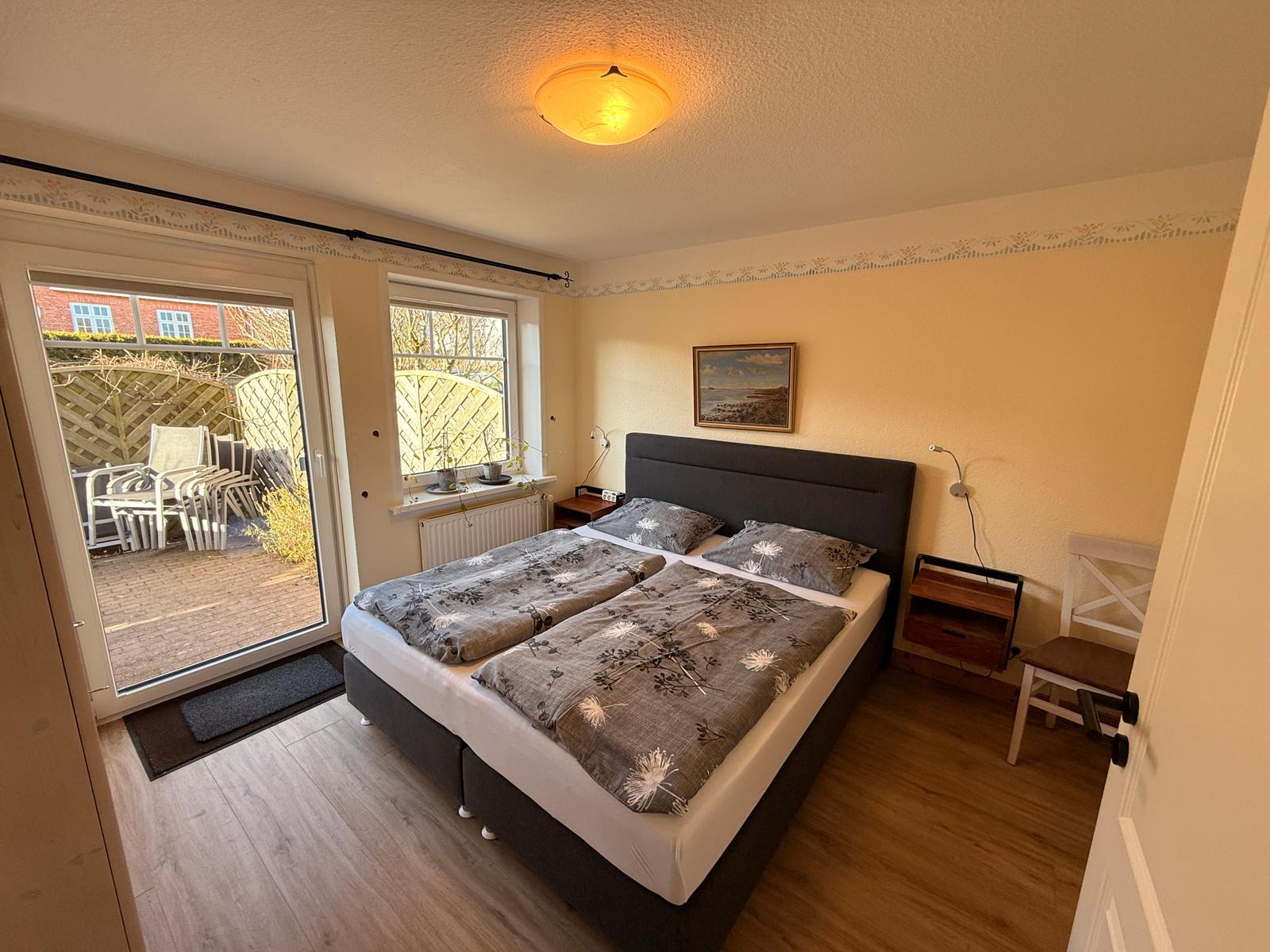 Schlafzimmer mit Doppelbett, Fenster und Glastür zum Garten.