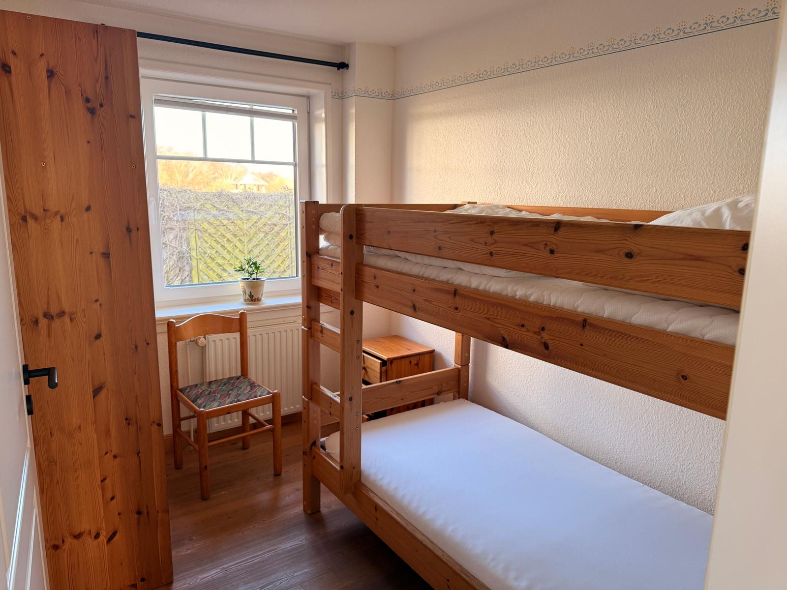 Zimmer mit Doppelstockbett, Holzstuhl und Fenster mit Blick auf Garten.
