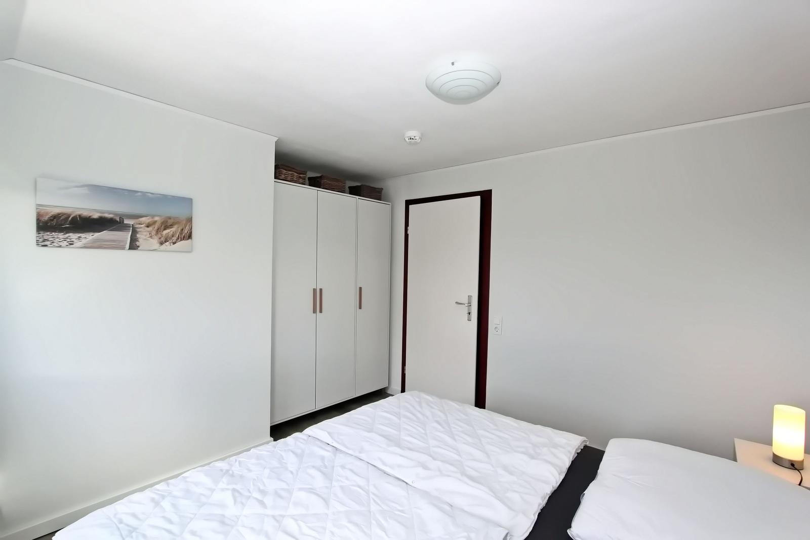 Schlafzimmer mit Bett, Schrank und Wandbild. Deckenleuchte und Nachttischlampe.