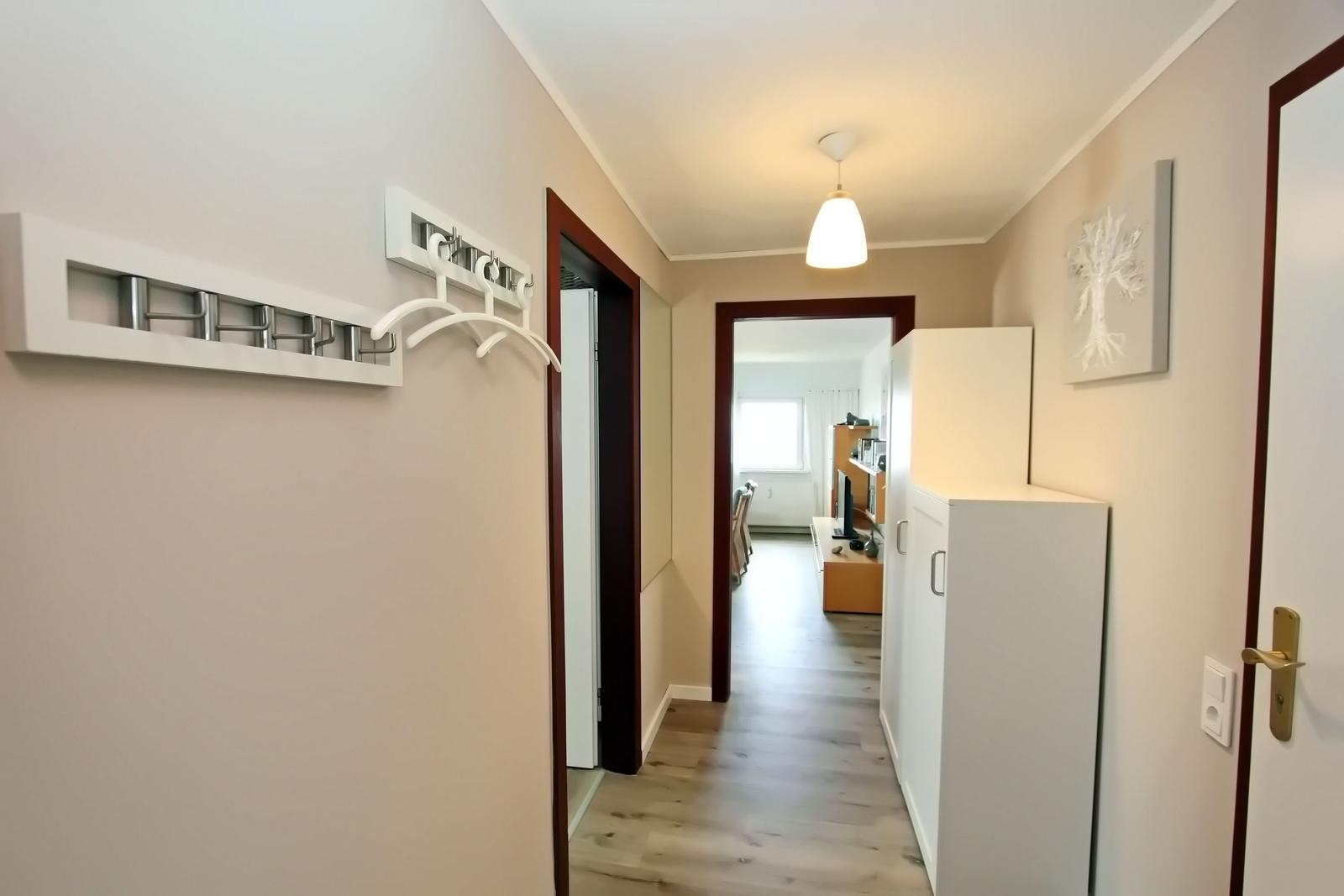 Flur mit Kleiderhaken, Schrank und Blick in Wohnbereich mit Fenster.