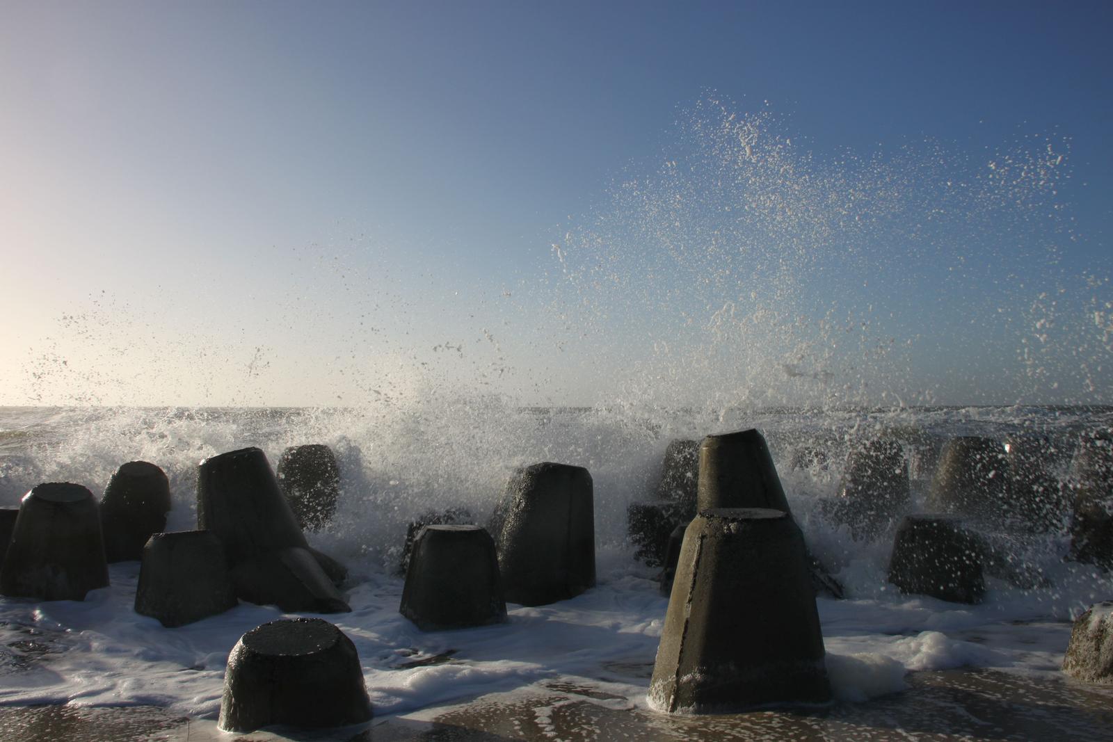 Wellen brechen an Betonblöcken am Strand.