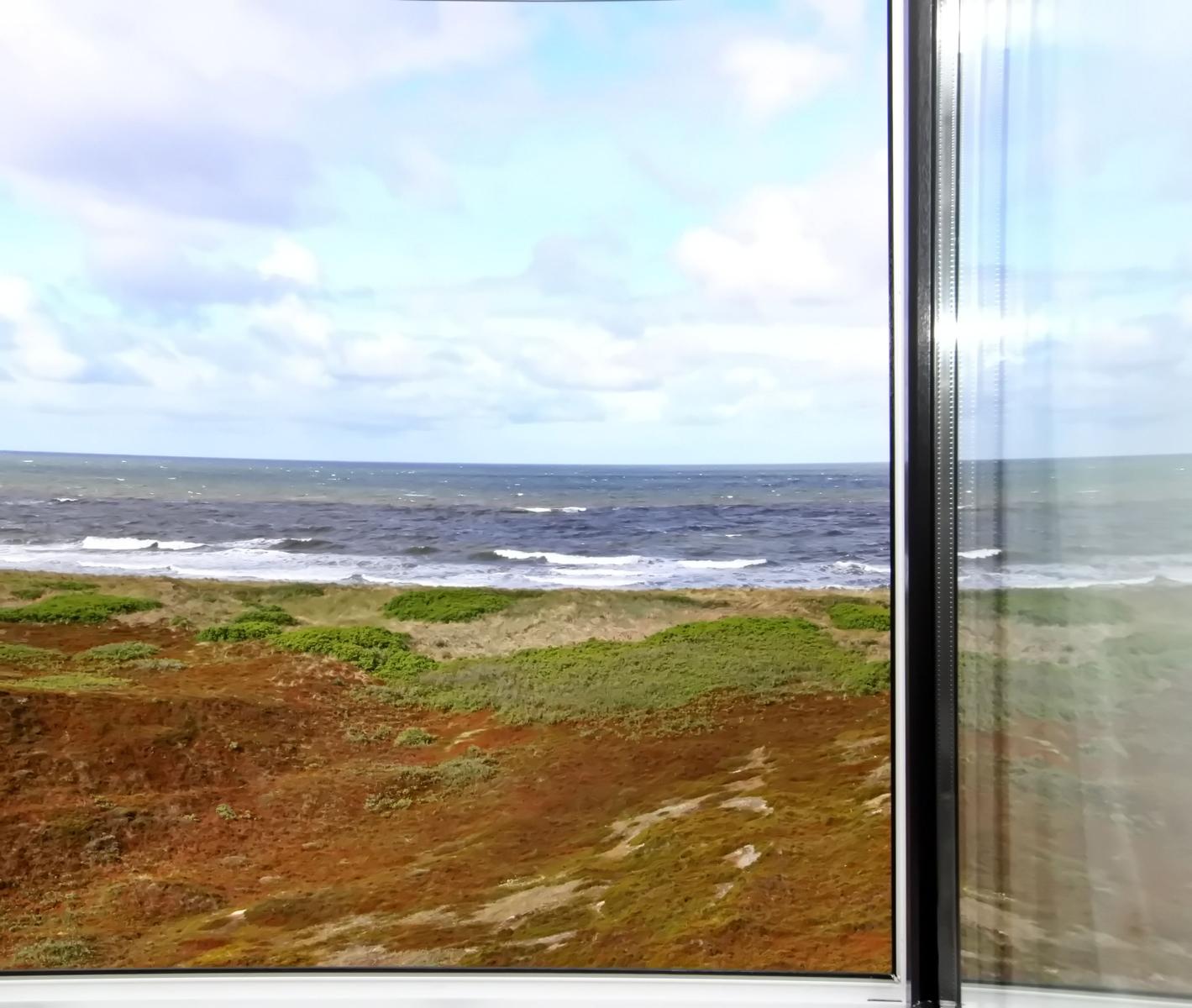 Blick auf das Meer und Küstenlandschaft durch ein Fenster.