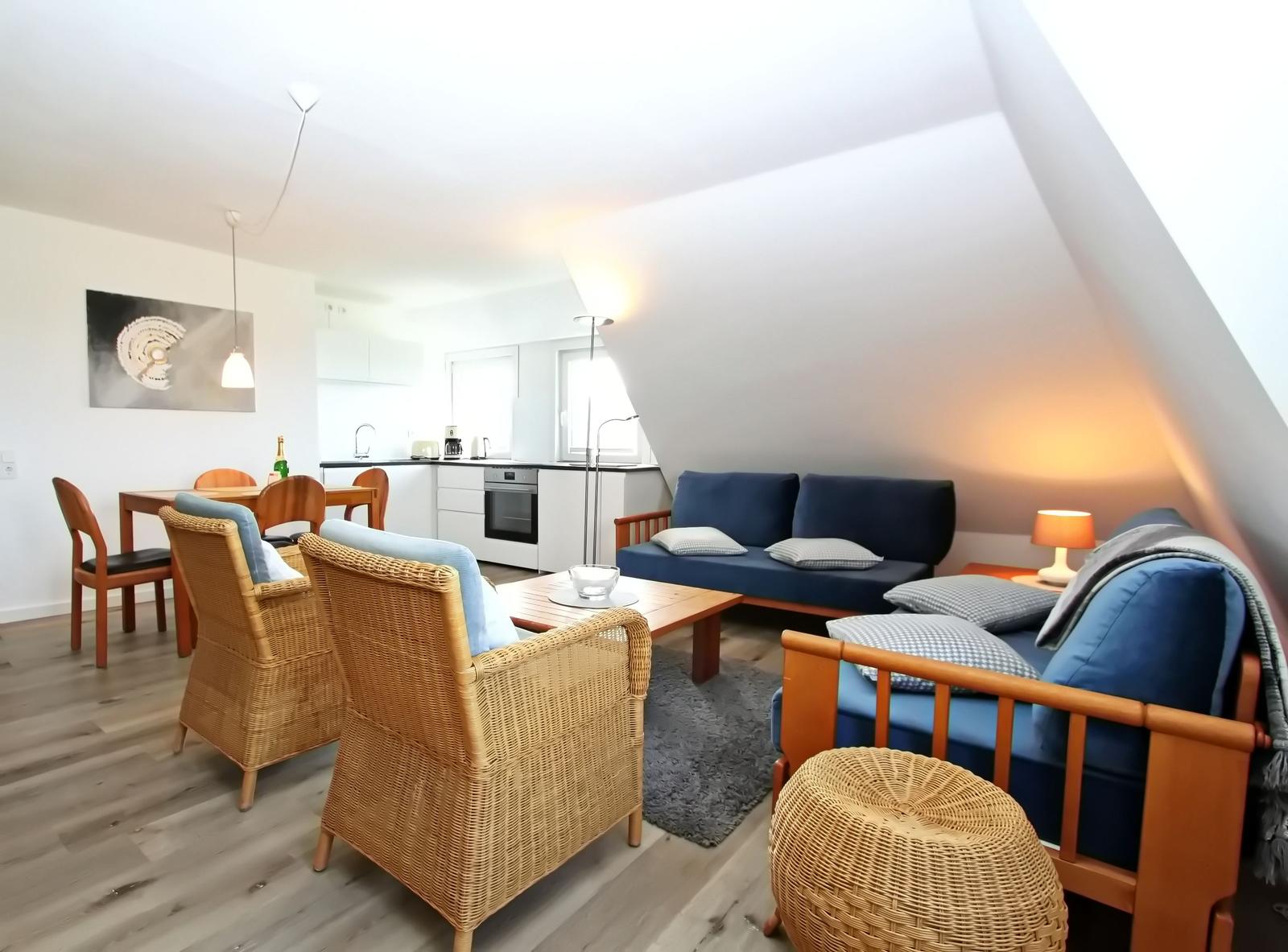 Wohn- und Essbereich mit Sofa, Stühlen und Küchenzeile unter Dachschrägen.