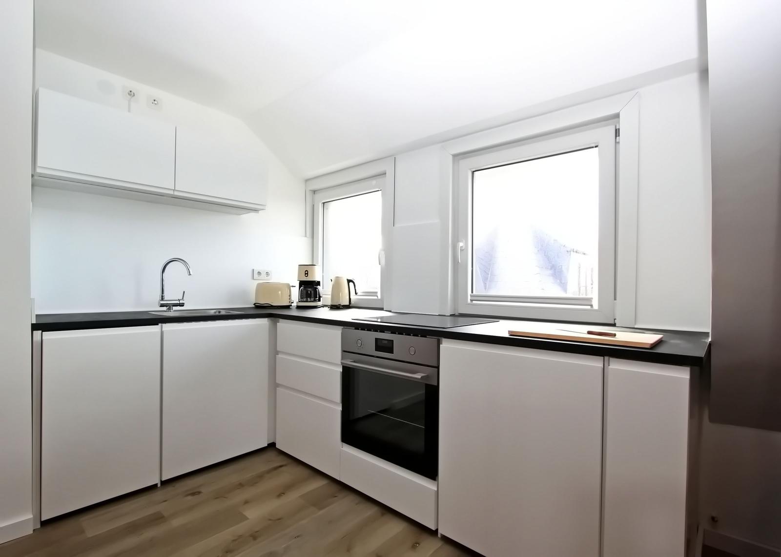 Küche mit weißen Schränken, schwarzer Arbeitsplatte und Fenster.