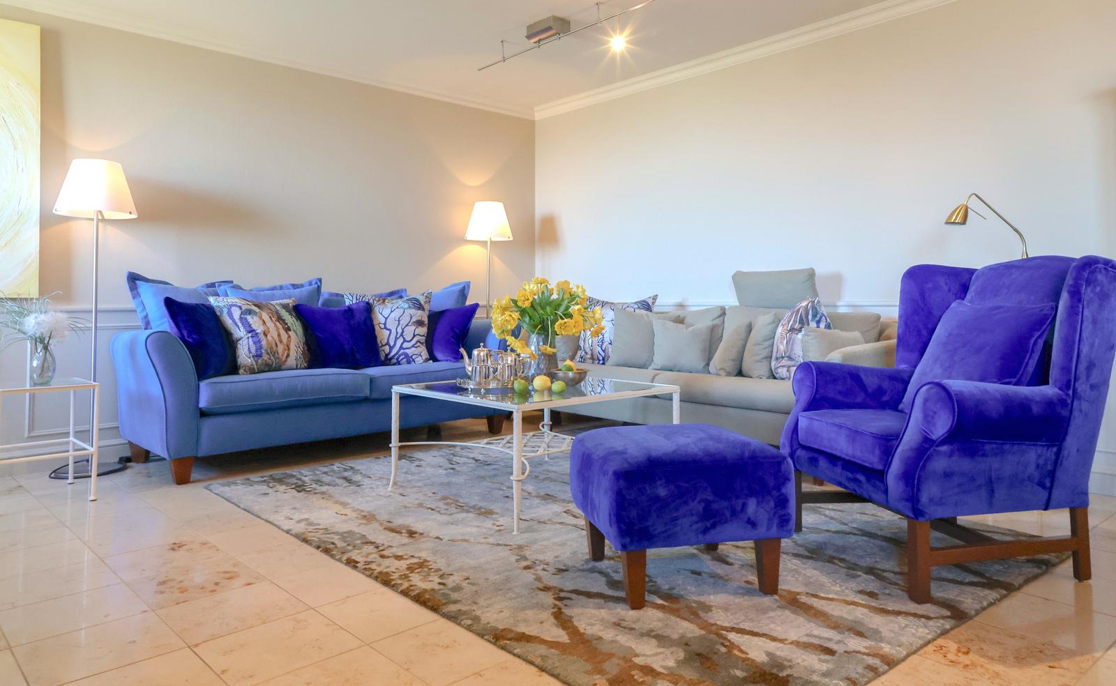 Wohnzimmer mit blauem Sofa, violettem Sessel und Glas-Tisch.