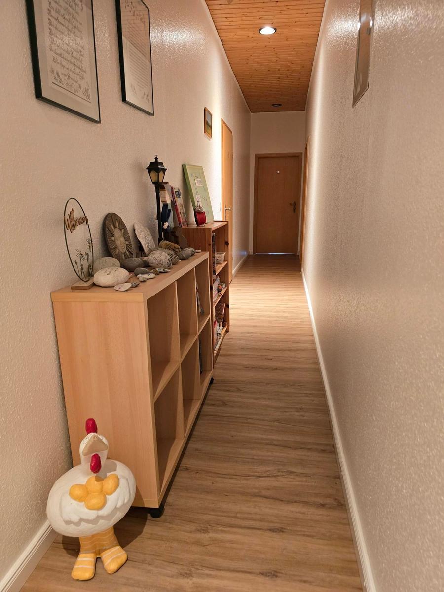 Flur mit Holzregal, dekorativen Gegenständen und einem Hühnchenfiguren.