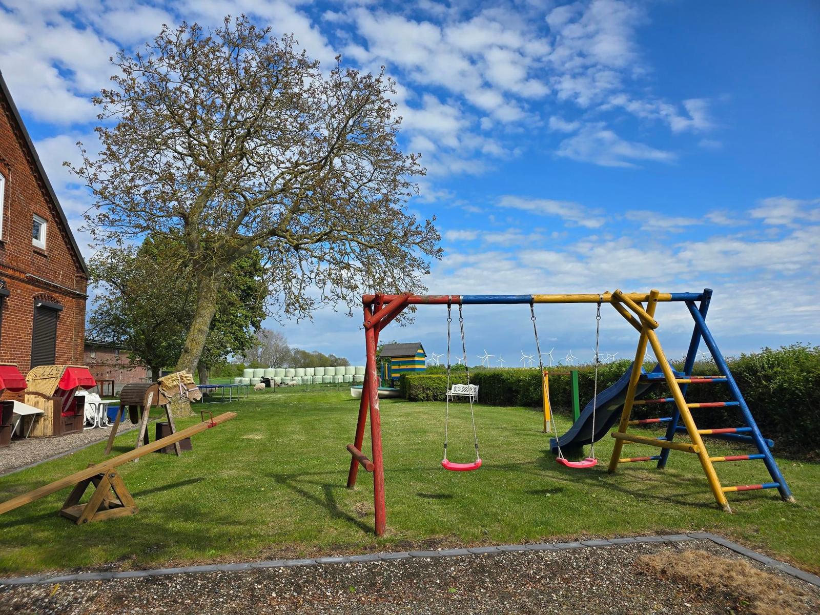 Kinderspielplatz mit Schaukel, Rutsche und Klettergerüst auf grünem Rasen.