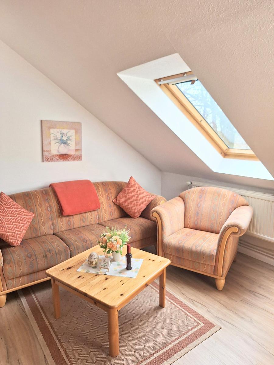 Wohnzimmer mit Sofa, Sessel und Tisch unter Dachschrägen mit Dachfenster.