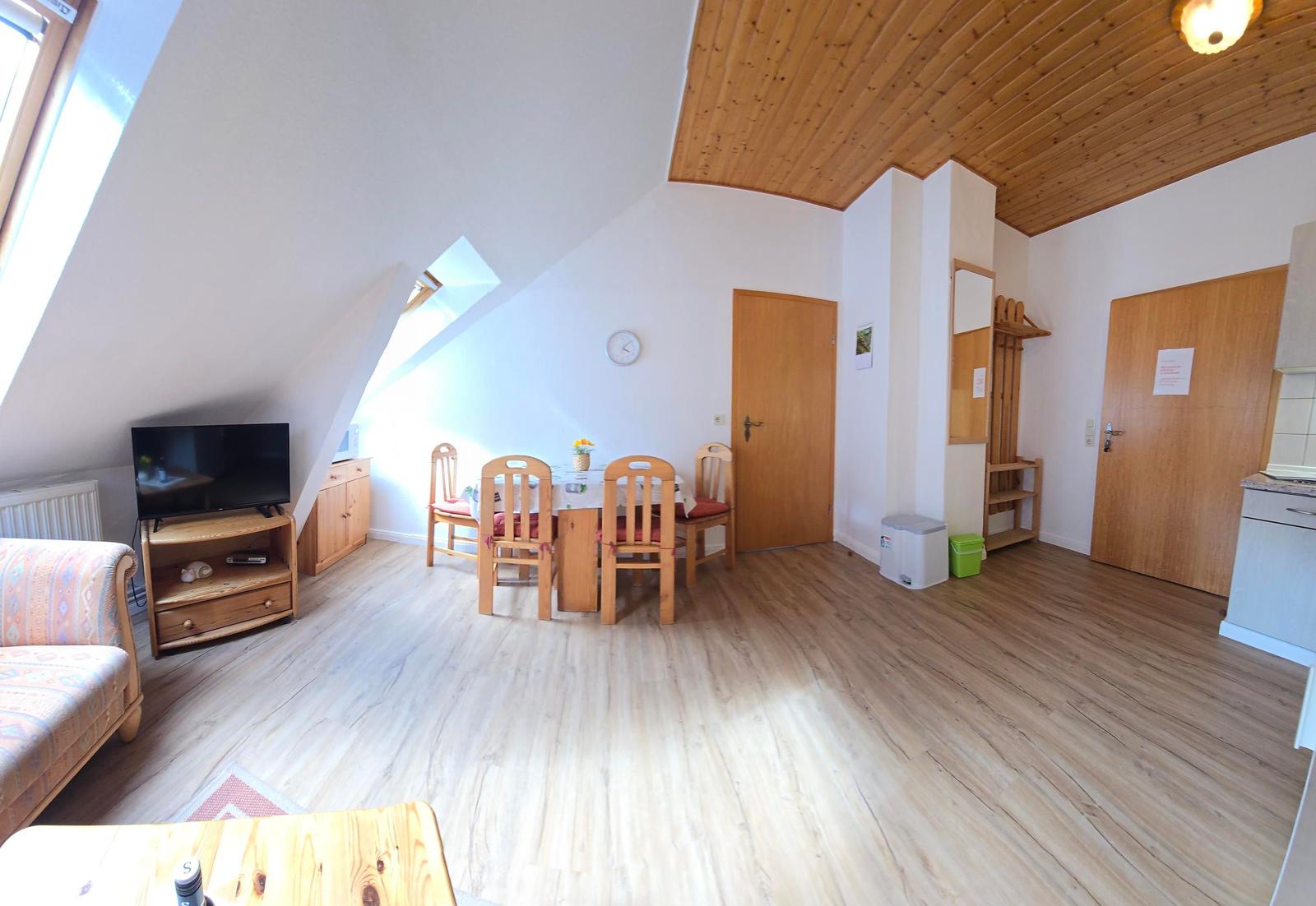 Wohn- und Essbereich mit Holzboden, Dachschrägen und TV. Essgruppe mit Tisch und Stühlen.