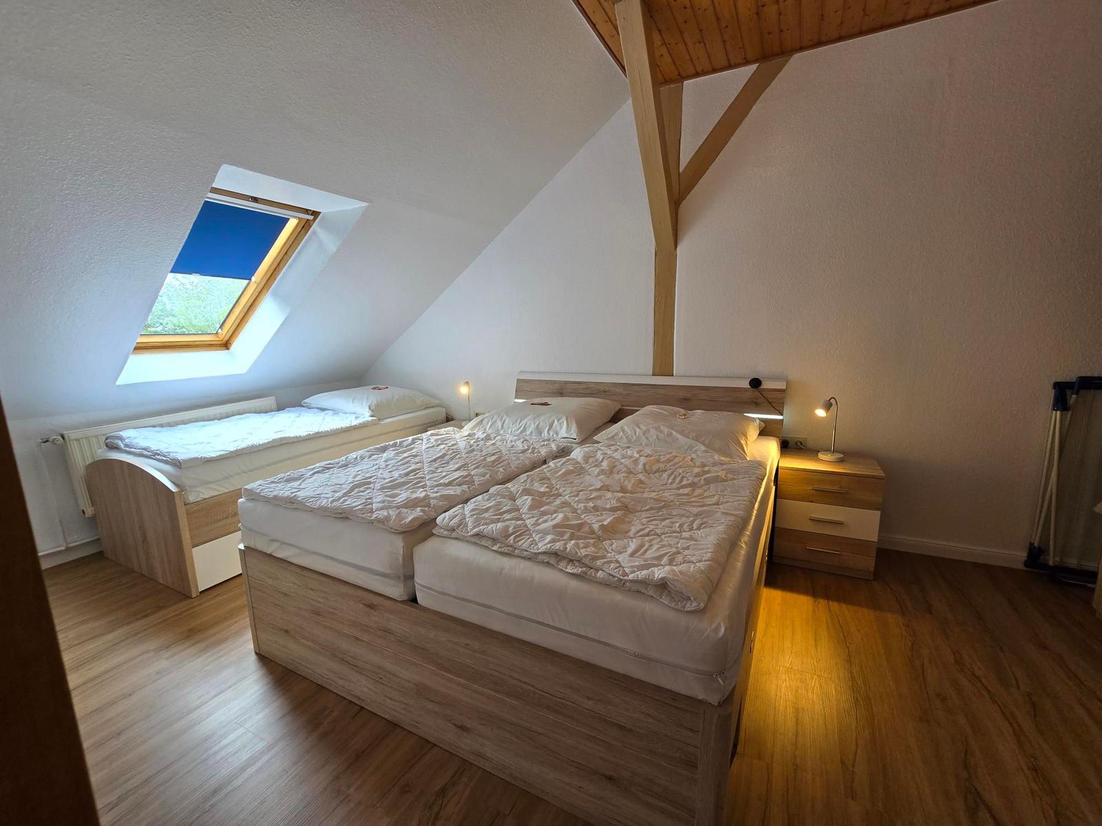 Schlafzimmer mit Doppelbett, kleinem Bett und Dachfenster.