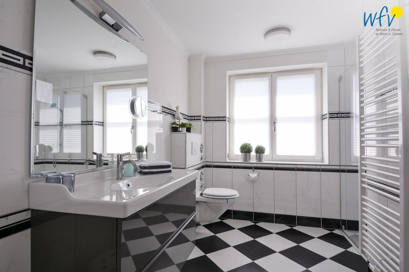 Badezimmer mit Waschbecken, Toilette und Dusche. Schwarze und weiße Fliesen.