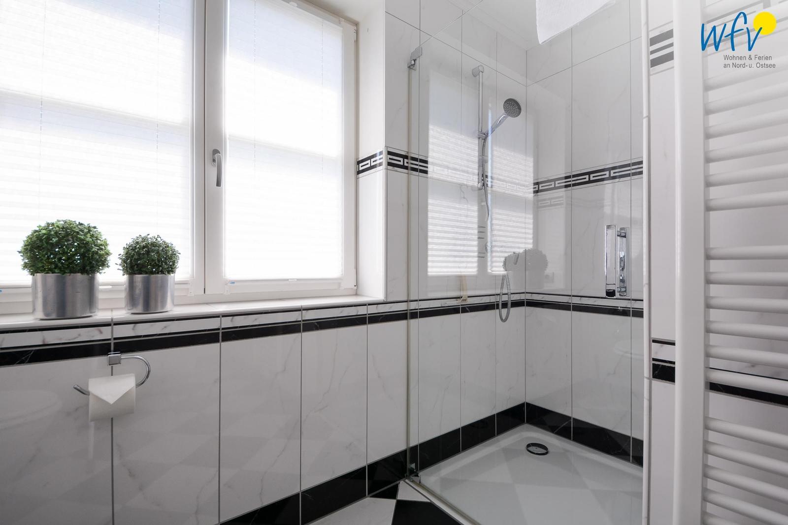 Badezimmer mit Dusche, Fenster und zwei Pflanzen auf der Fensterbank.