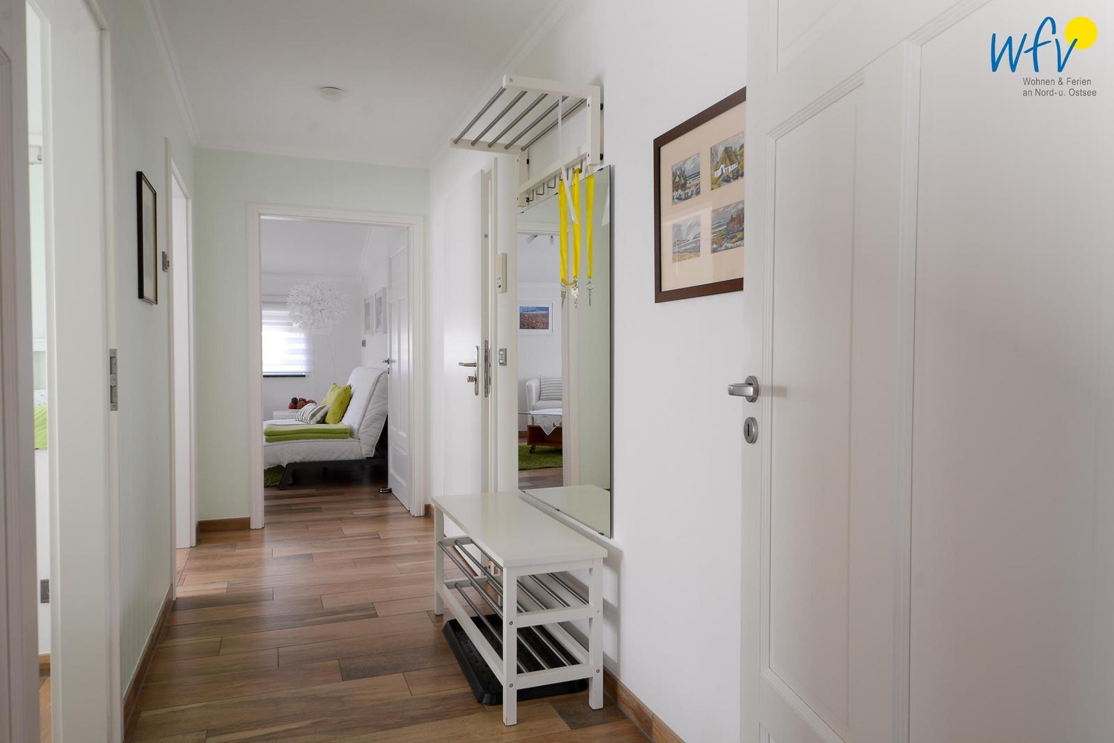 Flur mit Holzboden, Spiegel, Garderobe und Blick in Schlafzimmer und Wohnbereich.
