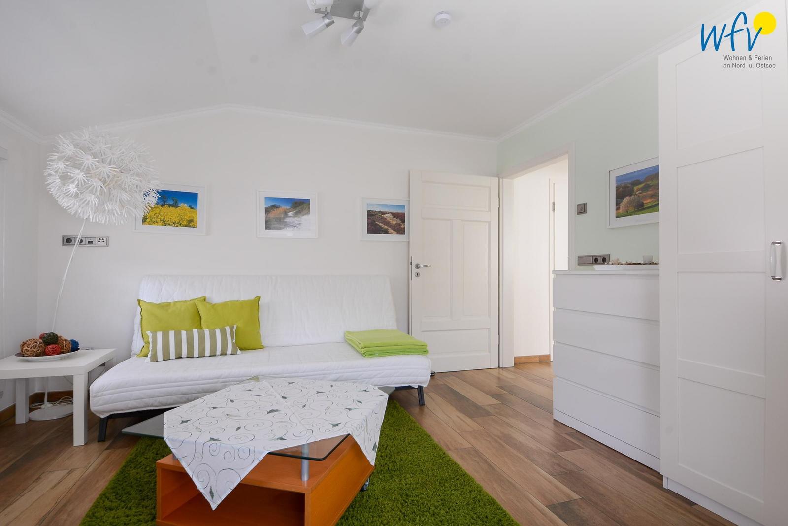 Wohnzimmer mit weißem Sofa, grünem Teppich und Holzboden.