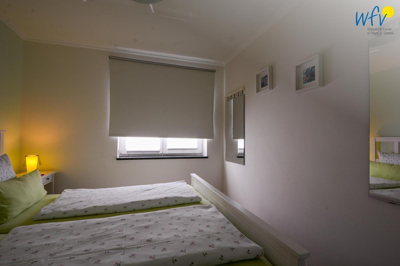 Zimmer mit zwei Betten, Fenster und Wandspiegel.