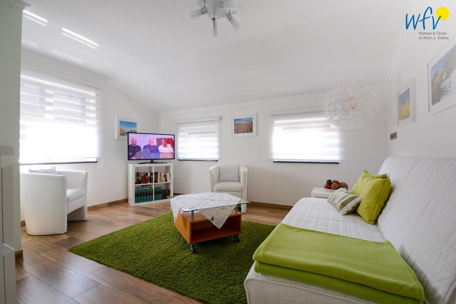 Wohnzimmer mit Sofa, Fernseher und grünem Teppich.