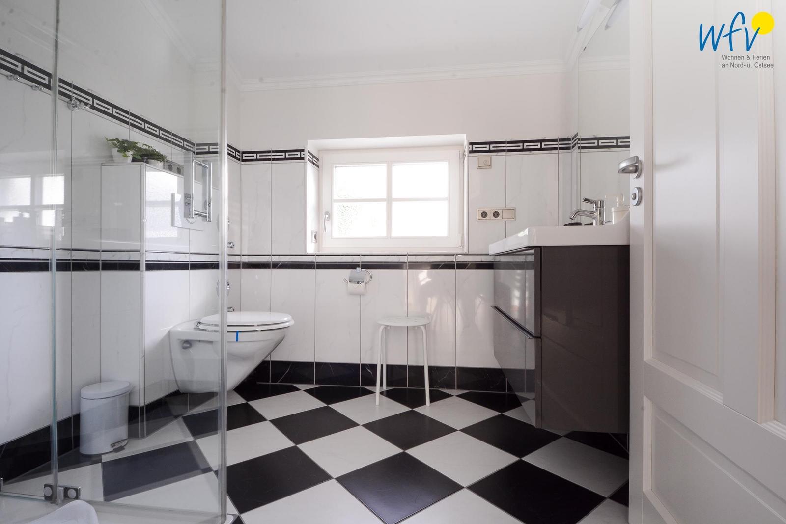 Badezimmer mit Dusche, Toilette und Waschbecken. Schwarze und weiße Fliesen.