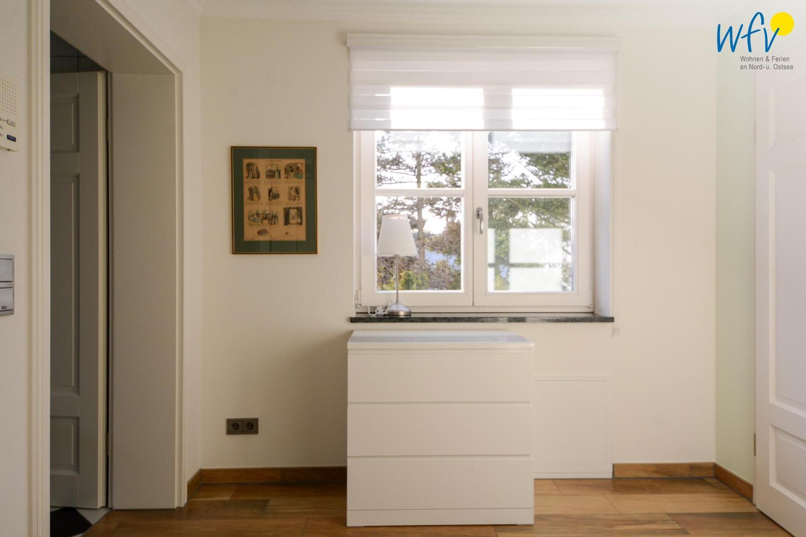 Ein Raum mit weißem Schrank, Fenster und Bild an der Wand.
